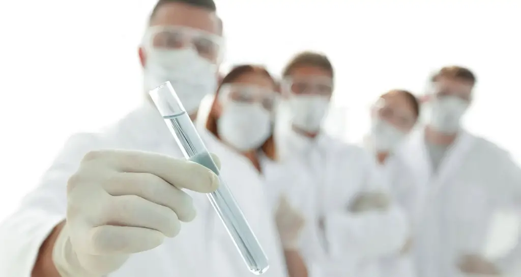 Lab scientist holding a test tube in focus, with a team of colleagues in the background, in a sterile environment for precise hair drug and alcohol testing