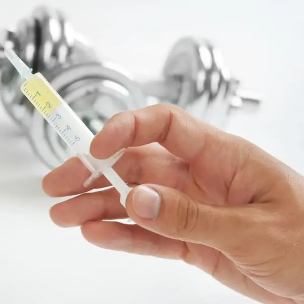 Close-up of a hand holding a syringe in a gym setting, highlighting the precision in steroid drug testing for athletes