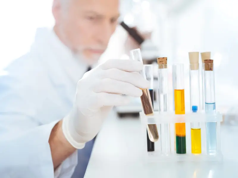 Laboratory scientist selecting a hair sample test tube from a rack of labelled specimens