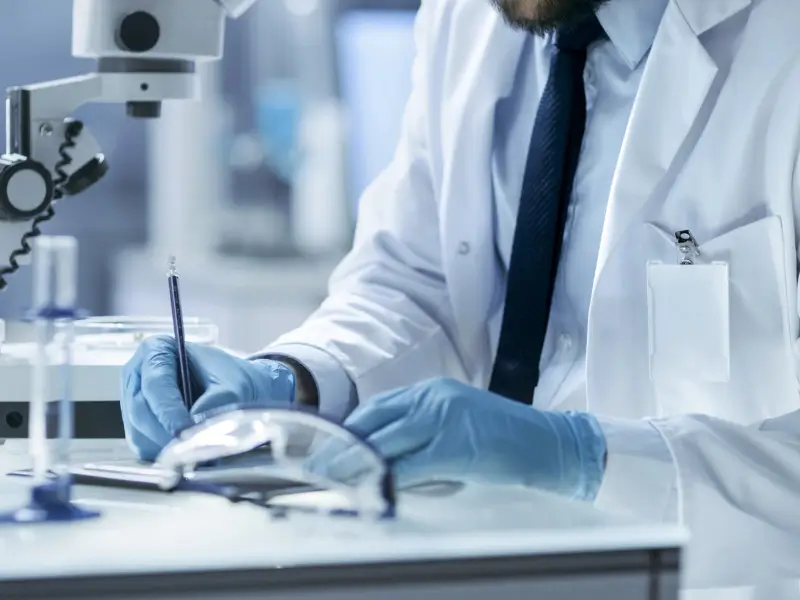 Laboratory scientist recording segmental hair sample results next to a microscope