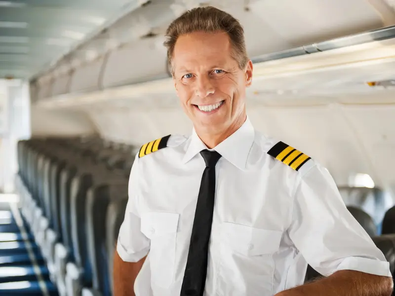 Airline pilot in uniform standing in the aircraft cabin, smiling at camera